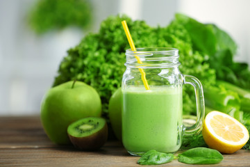 Mason jar of green healthy juice with vegetables and fruits on wooden table