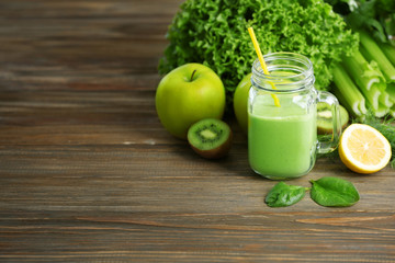 Mason jar of green healthy juice with vegetables and fruits on wooden table