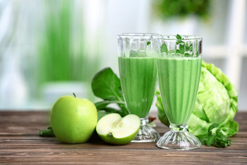 Glasses of green healthy juice with ingredients on wooden table