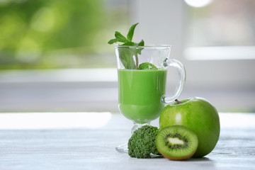 Glass of green healthy juice with ingredients on wooden table