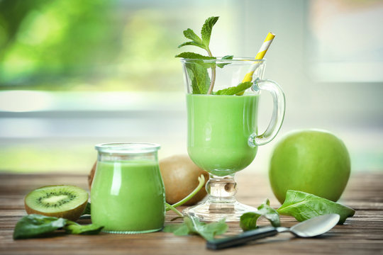 Glass and jar of green healthy juice with fruits on wooden table