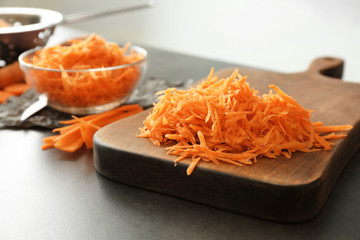 Wooden board with heap of grated carrot on kitchen table