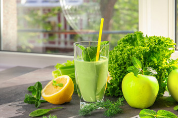 Glass of green healthy juice with fruits and vegetables on table