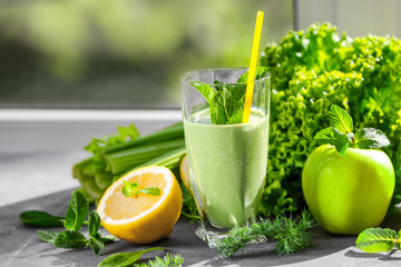 Glass of green healthy juice with fruits and vegetables on table