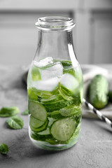 Delicious refreshing water with mint and cucumber in glass bottle on table