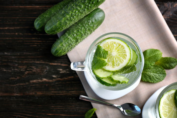 Delicious refreshing water with mint and cucumber in cup on wooden table