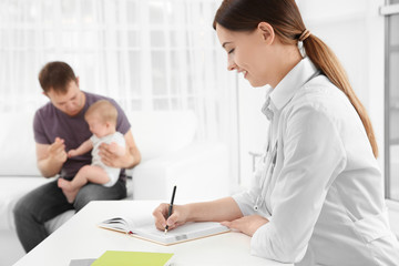 Fototapeta premium Doctor writing something in notebook and father with baby in hospital