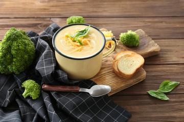 Cup with broccoli cheddar soup on wooden board