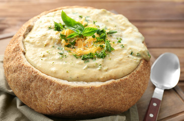 Broccoli cheddar soup in bread bowl on wooden board