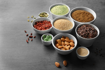 Composition with assortment of superfood products in bowls on grey table