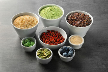Composition with assortment of superfood products in bowls on grey table