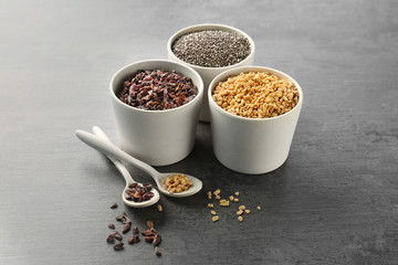 Composition with assortment of superfood products in bowls and spoons on grey table