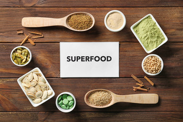 Composition with paper card and assortment of superfood products on wooden background