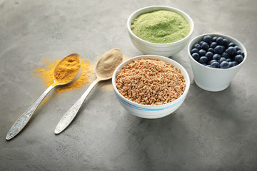 Composition with assortment of superfood products in bowls and spoons on grey textured background