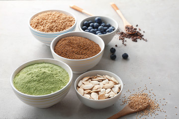 Composition with assortment of superfood products in bowls and spoons on light textured background