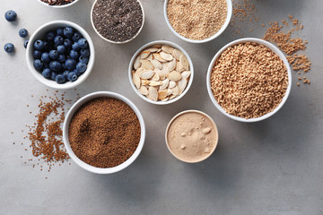 Composition with assortment of superfood products in bowls on light textured background, top view