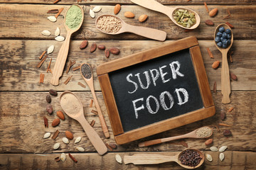 Composition with chalk board and assortment of superfood products in spoons on wooden background