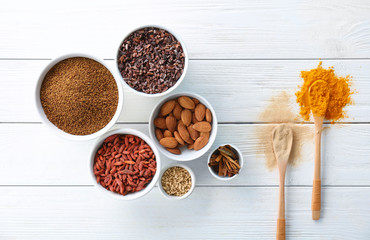 Composition with assortment of superfood products in bowls and spoons on light wooden background, top view