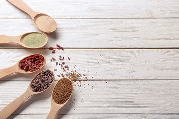 Composition with assortment of superfood products in wooden spoons on light table, top view