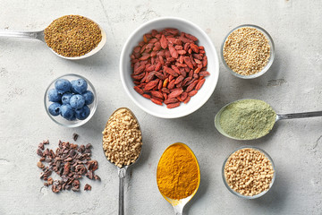 Composition with assortment of superfood products in bowls and spoons on light table