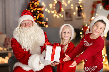 Santa Claus giving present to children in room with beautiful Christmas decorations