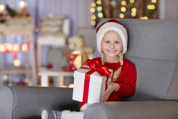 Cute little girl with Christmas gift box sitting in armchair at home
