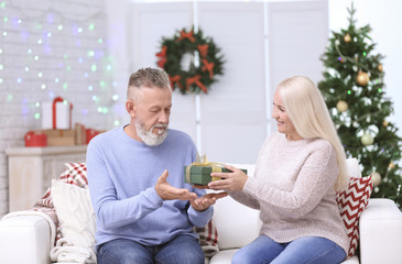 Senior woman giving Christmas present to her husband at home