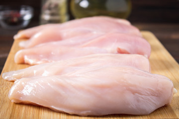 Raw chicken fillets on a cutting board against the background of a wooden table. Meat ingredients for cooking.