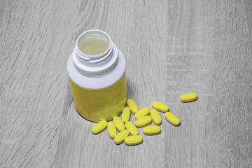 Yellow pills with pill bottle on wooden background