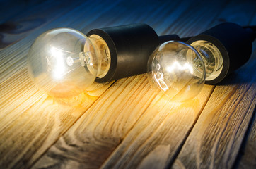 Two burning incandescent bulbs on a wooden table. Background with an empty space for your text