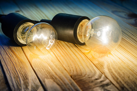 Two burning incandescent bulbs on a wooden table. Background with an empty space for your text