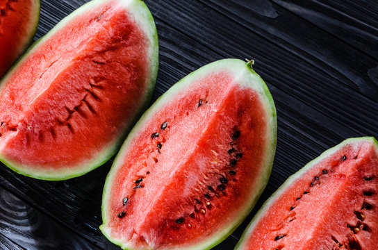 Background of fresh ripe watermelon slices on black wooden table. Top view.