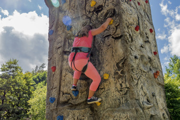 Fototapeta premium Young girl practicing rock climbing on artificial outdoor climbing wall. With sun flares.