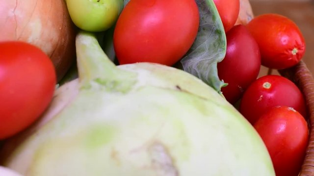 Cucumbers, onions, garlic, tomatoes, kohlrabi and pepers in wicker basket on brown backround. Rotating vegetables.