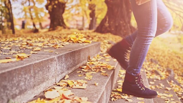 Unrecognizable Woman Feet walking Down the Stairs covered with Leaves in Autumn Park. 4K DOLLY SHOT, Close up on shoes. Girl enjoying cool fall weather outdoors, wearing stylish fall boots. 