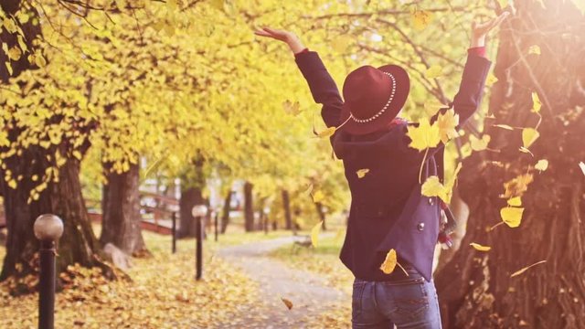 Happy Young Woman throwing leaves in Autumn Park. SLOW MOTION 120 FPS. Joyful and excited girl having fun enjoying sunny fall outdoors. 