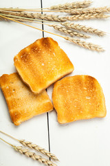 Toasts and wheat on a white wooden background