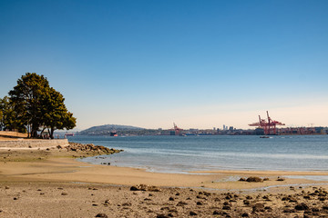 A beach in the foreground with cranes and Howe Sound in the background