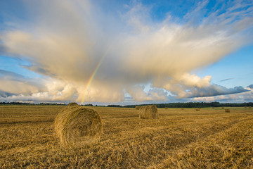 Finite field after harvest, rainbow over a field of straw bales