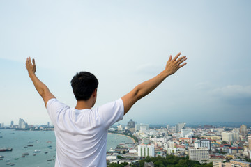 Fototapeta na wymiar young man happy with hands rise up on beautiful bay and city Landscape with beautiful cloudy sky, sea.