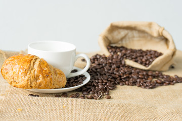 white cup of coffee with croissant and coffee beans (selective focus)