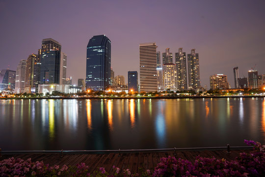 Asoke modern buildings of Bangkok night city skyline, Thailand. Cityscape photography of Benchakitti Park at dusk. Bangkok night city downtown. Modern night city skyline with lights reflection, Asia
