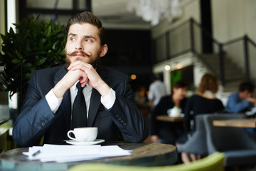Pensive businessman sitting in cafe by cup of coffee at break