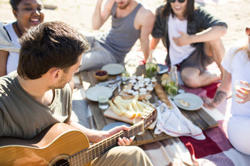 Young man playing guitar for his friends at picnic
