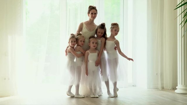 Teachers together with smoy schoolgirls are by the window of a ballet school. Little ballerinas run in embraces to the teacher