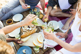 Young man with bottle of lemonade pouring it into glass of girl on picnic