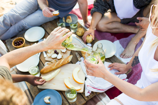 Young man with bottle of lemonade pouring it into glass of girl on picnic
