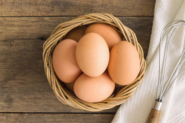 Fresh eggs in old wood basket put on white napkin. Prepare chicken eggs and egg whisk for cooking or bakery on rustic wood table.Top view, flat lay of eggs with copy space for background or wallpaper.