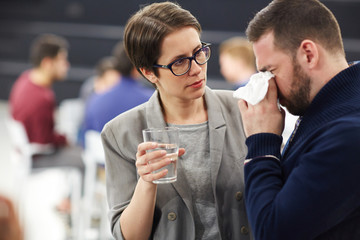 Helpful woman offering glass of water to crying man