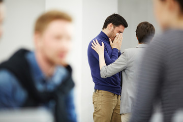 Fototapeta premium Young man crying while groupmate touching his shoulder and sharing his pain